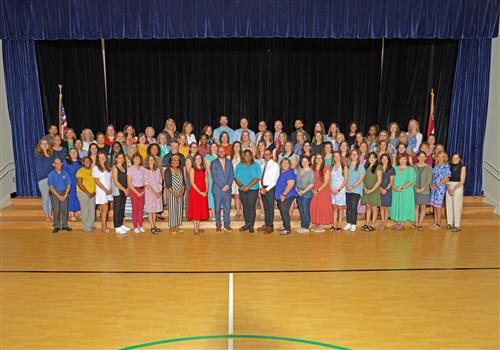 Entire school staff on the steps of the stage against a blue curtain with flags